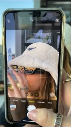 a person taking a photo with their cell phone while wearing a white hat and sunglasses