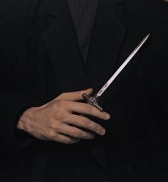 a man in a black suit holding a knife and wearing a ring on his finger