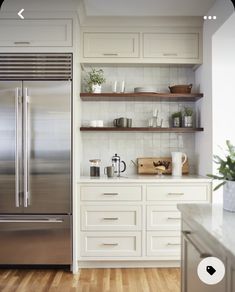 a stainless steel refrigerator in a white kitchen with open shelving and wooden flooring