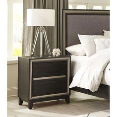 a night stand with a lamp on it next to a bed