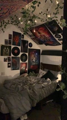 an unmade bed in a room with pictures on the wall and plants hanging from the ceiling