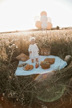 a baby is sitting on a blanket in the middle of a field with some bread