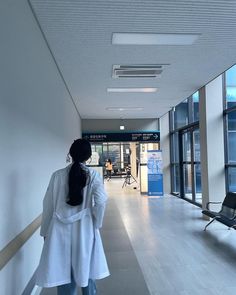 a woman walking down a hallway in an office building with lots of windows on both sides