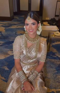 a woman sitting on the floor wearing a gold dress and necklace with flowers in her hair