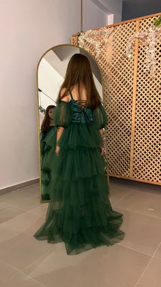 a woman standing in front of a mirror wearing a green dress with ruffles