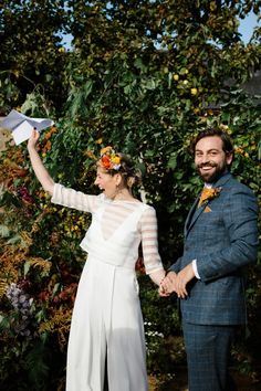 a man and woman holding hands while standing next to each other in front of trees