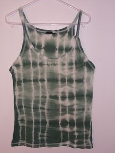 a tank top hanging on a hanger in front of a white wall with a black and green tie - dye pattern