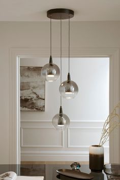 three glass globes hang from the ceiling above a dining room table with two vases on it