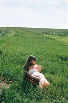 a woman sitting in the middle of a field holding an acoustic guitar and looking into the distance