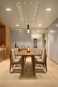 a dining room table with white chairs and lights on the ceiling above it, in front of an open living area