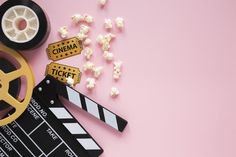 a movie clapper, film reel and popcorn on a pink background