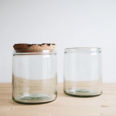 two glass jars sitting on top of a wooden table next to each other, one filled with sand and the other empty