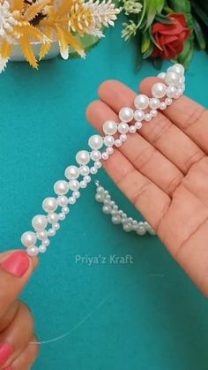 a hand holding a strand of pearls in it's left hand next to flowers