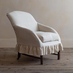 an upholstered chair with ruffles on the legs and back rests against a wall