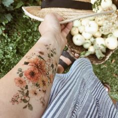 a person with a flower tattoo on their arm holding a straw hat in front of some vegetables