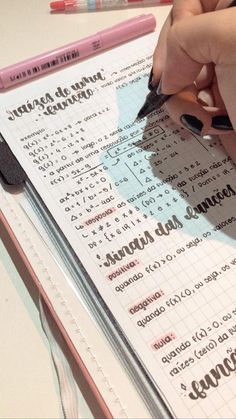 a person writing on a piece of paper next to a pink pen and two markers