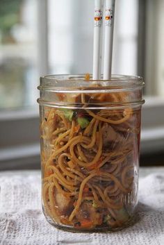 a glass jar filled with noodles and carrots on top of a table next to a window