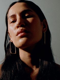 a woman with her eyes closed wearing large gold hoop earrings and black dress, looking up at the sky