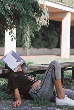 a person laying on the ground with a book over their head and reading a book