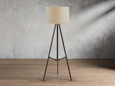 a floor lamp with a white shade on it in front of a gray wall and wooden floor