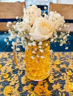 a beer mug filled with white flowers on top of a blue and yellow table cloth