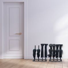 five black vases are lined up in front of a white wall and wooden floor