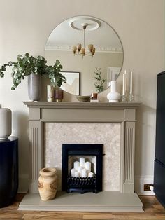 Olive green wooden fireplace suround. Marble with black fire insert. Round mirror. Vase of eucalyptus.