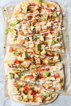 an uncooked pizza with chicken, tomatoes and avocado on parchment paper