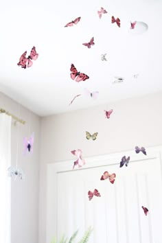 a white room with pink and purple butterflies hanging from it's ceiling, next to a potted plant