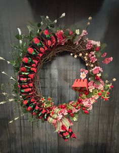 a wreath with red flowers and green leaves hanging on a wooden wall in front of a door