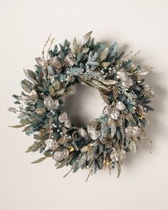 a wreath hanging on the wall with silver and green leaves, berries and pine cones