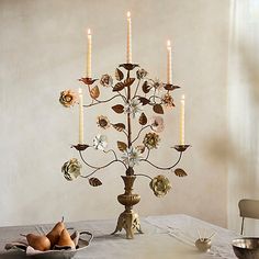 a table topped with a vase filled with flowers next to candles and fruit on top of it