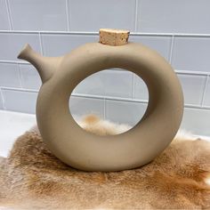 a vase sitting on top of a fur rug in front of a white tile wall