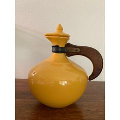 a yellow vase sitting on top of a wooden table next to a wall with a brown handle