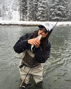 a woman standing in the water while holding a fish and fishing pole with her mouth open