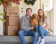 a man and woman sitting on the steps with their dog in front of boxes that say it's official