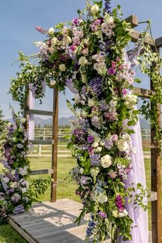 an outdoor ceremony with purple and white flowers on the arbor, along with greenery