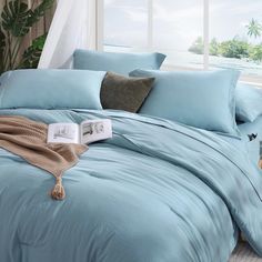 a bed with blue comforters and pillows on it in front of a large window