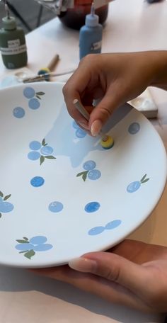 two hands are holding a plate with blue flowers on it and one hand is using a knife