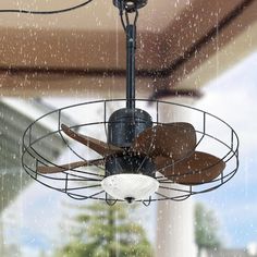 a ceiling fan that is hanging from the ceiling in front of a window with rain falling on it