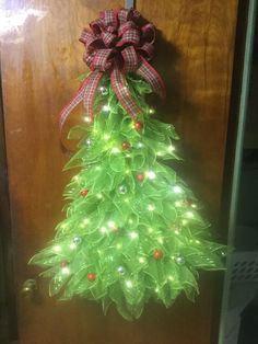 a green christmas tree with lights and a bow hanging from the front door, on a wooden door