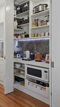 a kitchen with white cupboards and wooden floors is pictured in this image, there are many items on the shelves