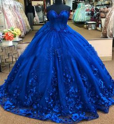 Embrace the magic of your quinceanera with this exquisite royal blue ball gown. The dramatic ball gown is crafted from luxurious tulle, and offers a voluminous, fairy-tale look, while the chapel train adds a regal flair, perfect for your grand entrance. The strapless neckline creates an elegant and timeless look, highlighting your shoulders and neckline with sophistication. What truly sets this gown apart are the stunning 3D flowers and applique detailing, which delicately adorn the bodice and s Floral Quince Dress, Royal Blue Princess Dress, Royal Blue Quince Dress, Floral Quince, Blue Quince Dress, Royal Blue Ball Gown, Royal Blue Quinceanera Dresses, Royal Blue Quinceanera, Blue Princess Dress