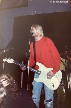 a man standing in front of a microphone while holding a guitar