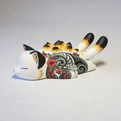 a cat figurine sitting on top of a white surface with black and orange designs