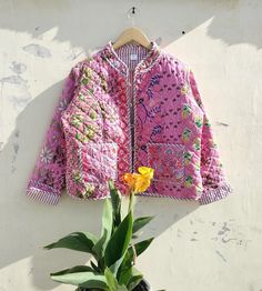 a small potted plant next to a pink jacket hanging on a wall with a yellow flower in it