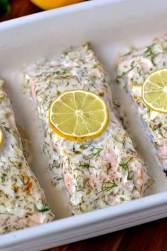 three slices of salmon with lemons and herbs on them in a white dish next to some lemon wedges