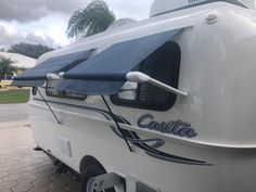 a white trailer with a blue awning on it's side and palm trees in the background