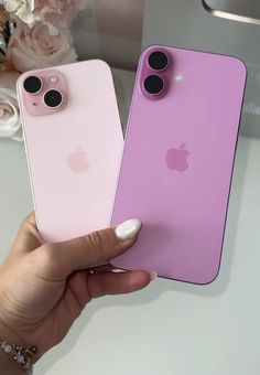 two pink iphones being held up in front of each other on a white table