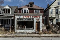 an abandoned candy store sits on the corner of a street in front of two older houses